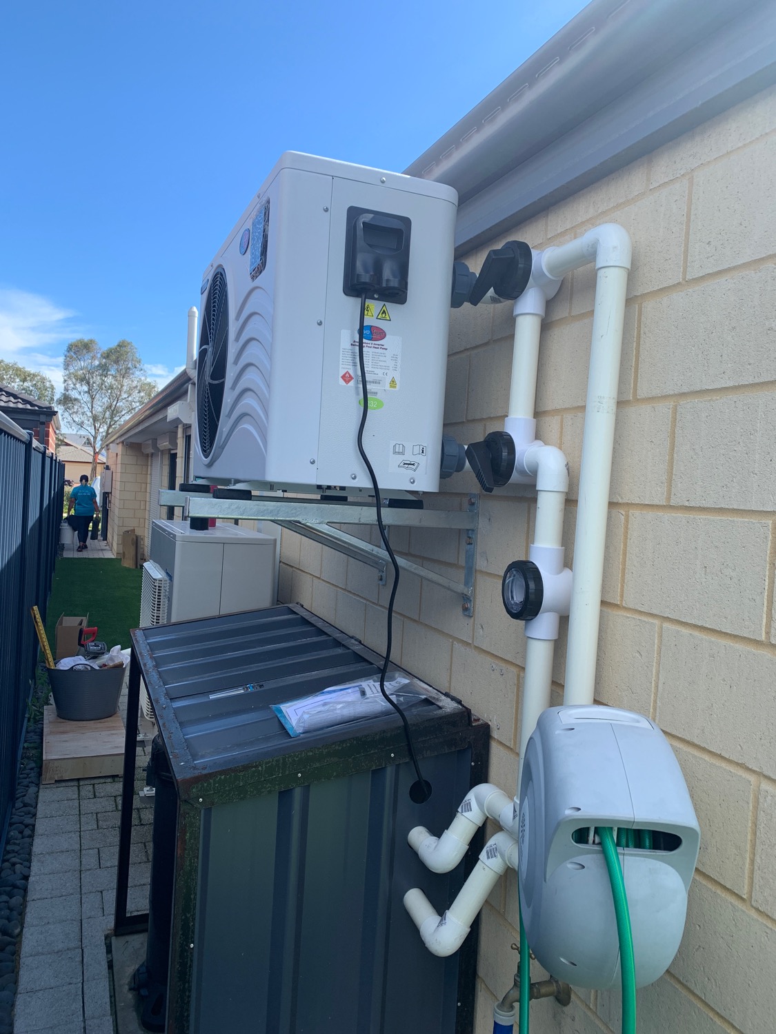 A heat pump mounted on brackets on a brick wall above the pool equipment