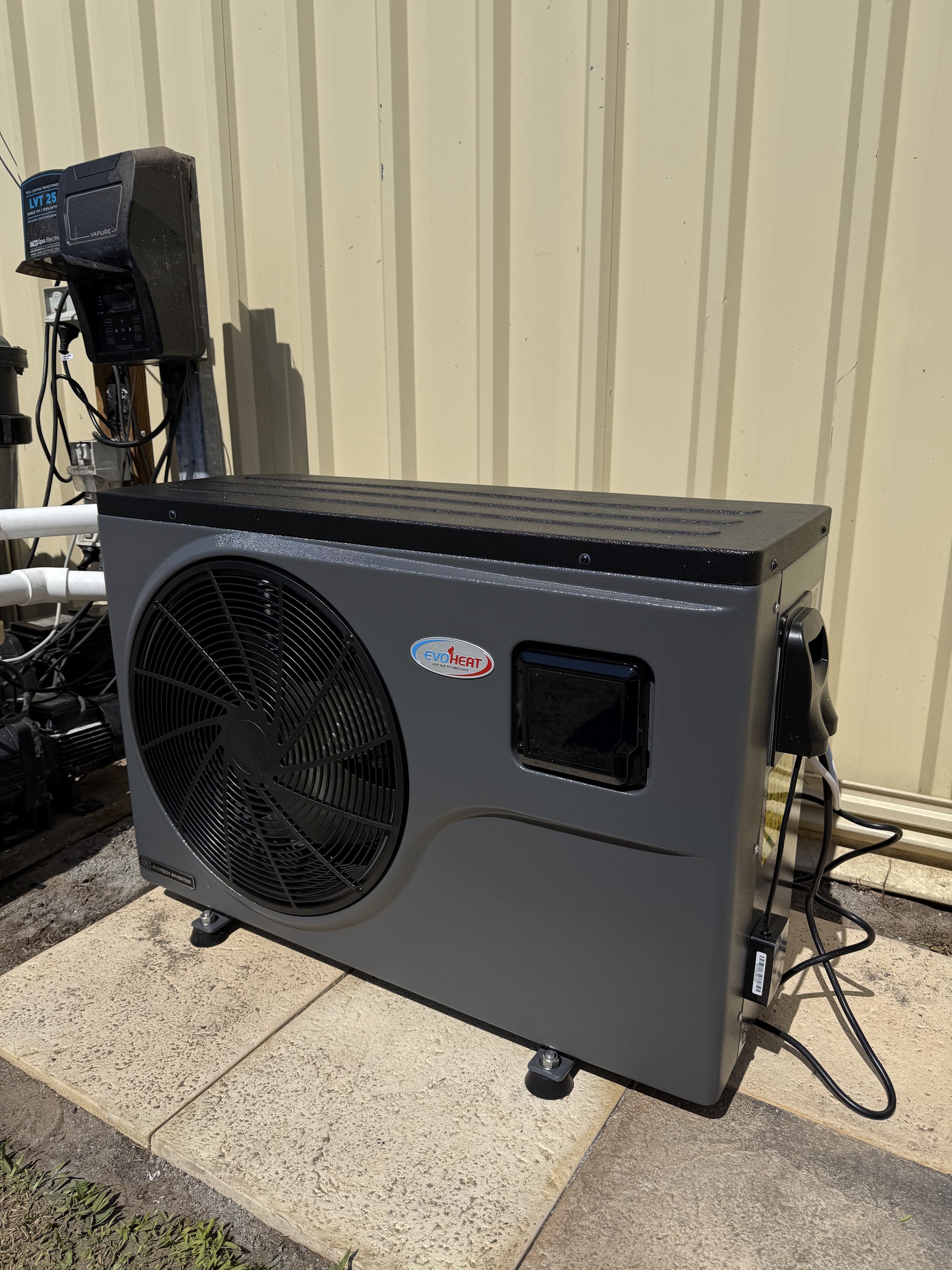 A charcoal pool heat pump on a paved pad