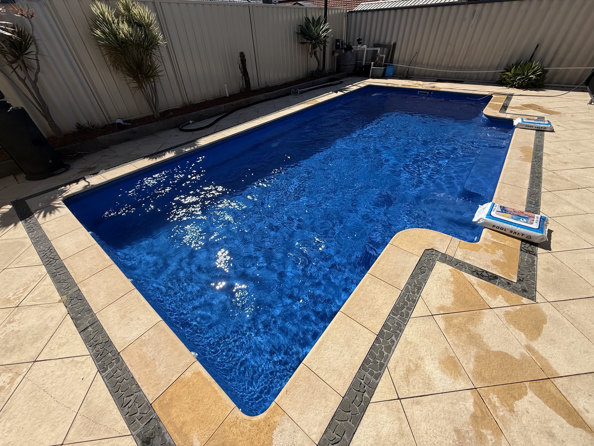 A freshly serviced in-ground pool with bright blue water and limestone paving