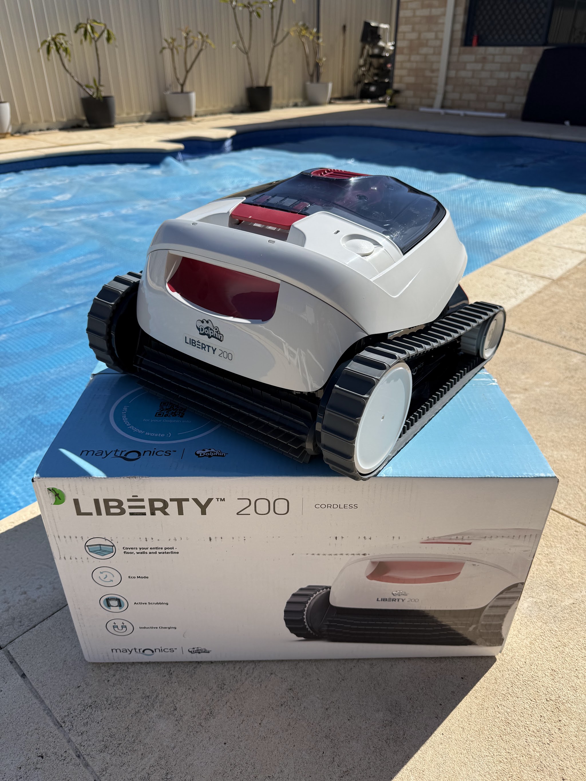 A Dolphin Liberty 200 cordless robotic pool cleaner on its box beside a pool